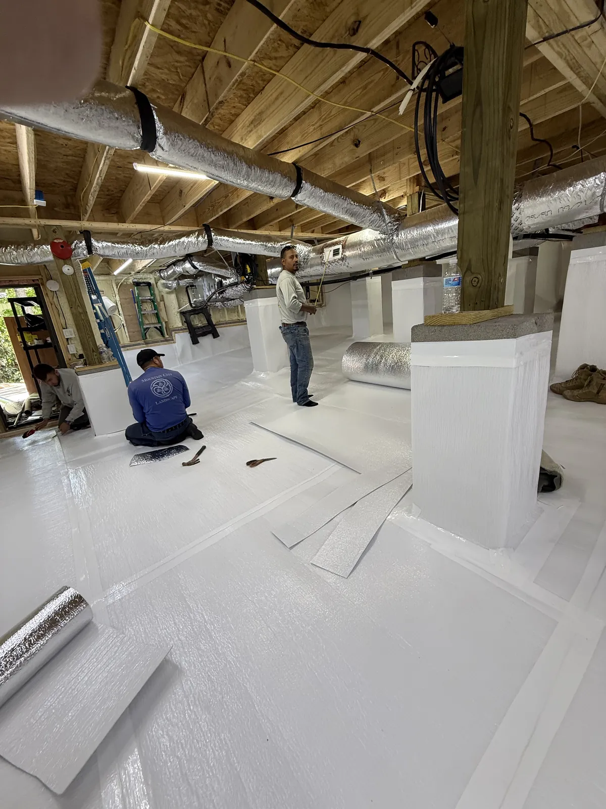 Crawlspace Doctor crew installing white vapor barrier liner around wrapped support columns during encapsulation, Hamilton County TN